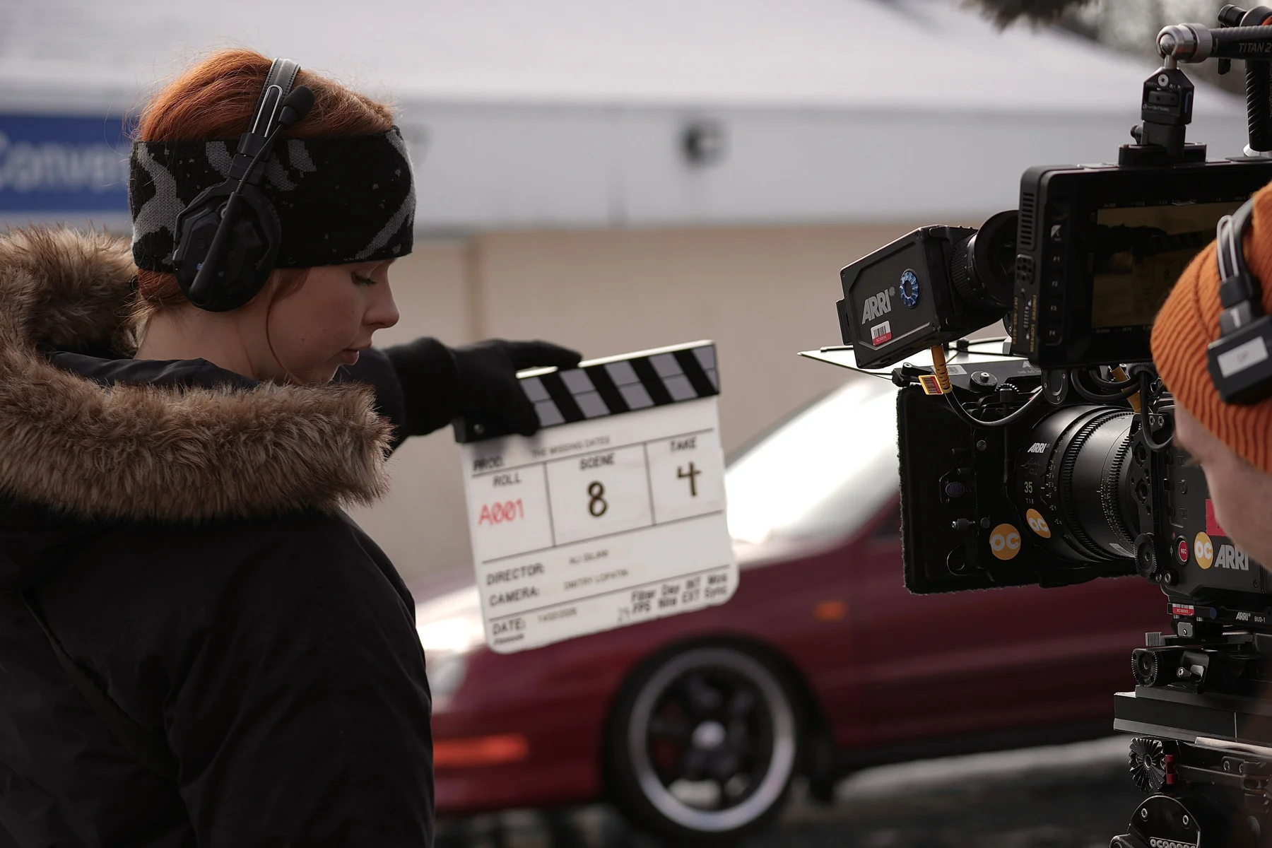A crew member holds the slate beside the camera and picture vehicle.